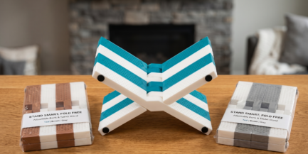 Foldable adjustable book and tablet stand in teal and white color displayed on a wooden table with packaged color variants beside it.